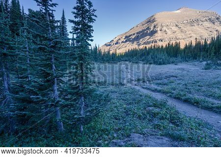 Morning Sun Lights Up A Peak While Meadows Are Still In A Shadow. Cold Sunny Morning In Glacier Nati