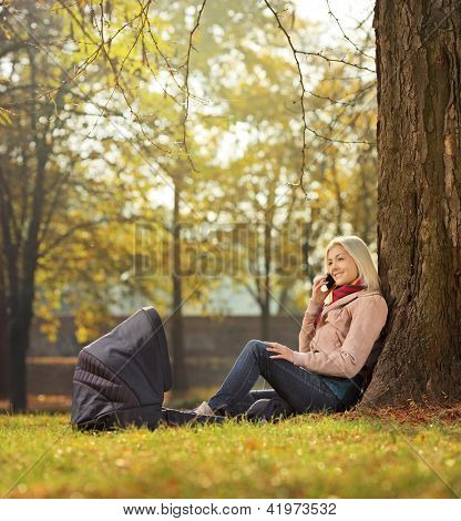 Bir Portbebe onu bebek ile bir parkta oturan ve bir cep telefonu konuşurken genç anne
