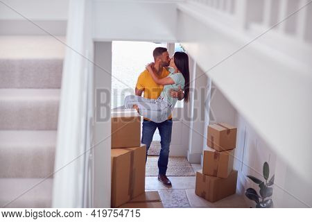 Man Carrying Woman Over Threshold Of New Home As Couple Move In Together