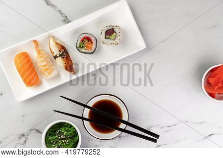 Nigiri sushi served on a white plate, seaweed salad and soy sauce on side on a white stone background. Traditional asian food, top view.