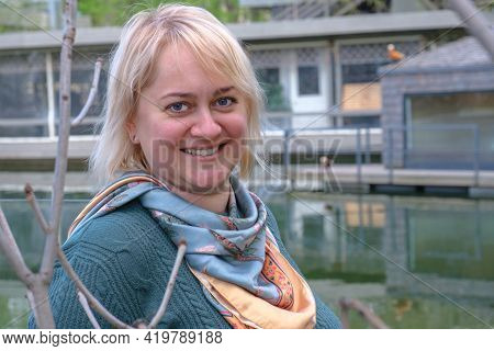 Portrait Of A Middle-aged Woman With Blond Hair Against The Backdrop Of A Pond And A Country House. 