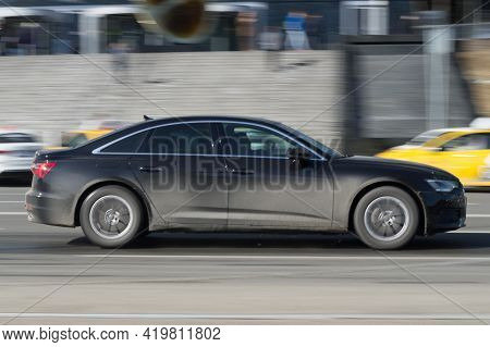 Man Texting On His Mobile Phone While Driving. Black Dirty Audi A6 C8 Is Driving Along The Street In