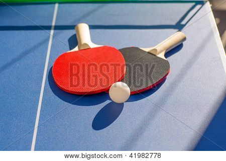 duas pás do tênis de mesa ping pong e a bola branca na placa azul