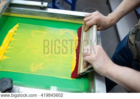 Serigraphy Silk Screen Print Process At Clothes Factory. Frame, Squeegee And Plastisol Color Paints.