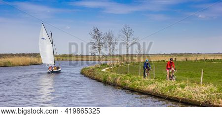 Friesland, Netherlands - April 27, 2021: Sailing Boat And Cyclists In The Landscape Of Friesland, Ne