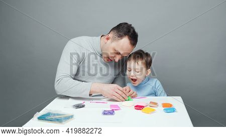 Photo Of Dad And Son Sculpting In Plasticine On Gray Background