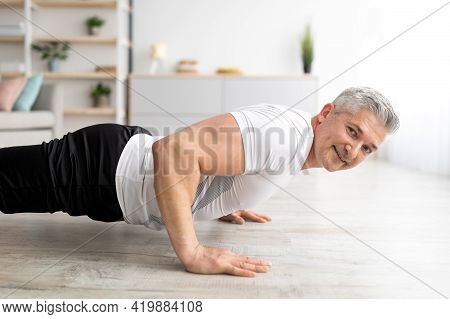 Active Lifestyle. Sporty Mature Man Doing Push-ups Or Plank Exercise On Floor, Exercising In Living 