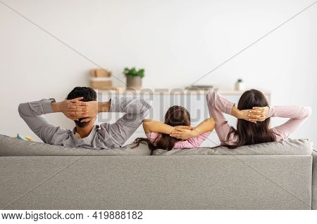 Leisure Time. Back View Of Relaxed Parents And Child With Arms Behind Head Sitting On Couch And Rest