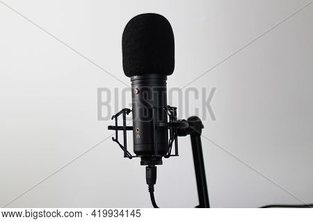 Generic cardioid microphone with pop filter and shock mount and live red led in a clean setting.