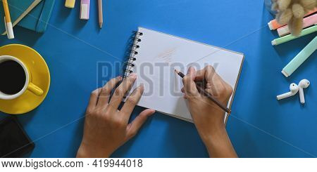 Top View Image Of Hands While Taking Note On Notebook That Putting On Colorful Working Desk And Surr