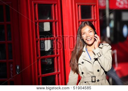 London woman taking on smart phone by red phone booth. Young casual female business woman walking with mobile phone smartphone in London, England, United Kingdom. Multiracial Asian Caucasian model.