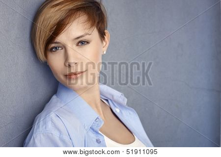 Closeup portrait of attractive young woman leaning to grey wall, looking at camera