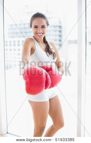 Cheerful sporty brunette wearing red boxing gloves in bright room