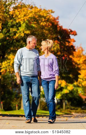 senior couple, Man and woman, having a walk in autumn or fall outdoors, the trees show colorful foliage