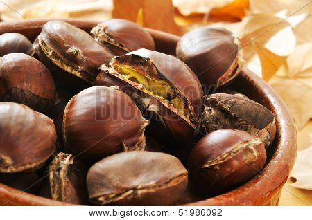 an earthenware bowl with roasted chestnuts and autumn leaves in the background