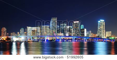 Miami city skyline panorama at dusk with urban skyscrapers and bridge over sea with reflection
