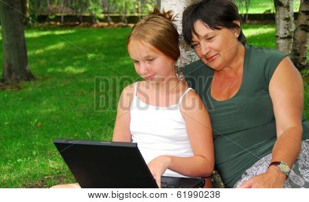 Grandmother and granddaughter sitting outside with laptop computer