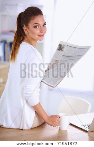 Cute businesswoman holding newspaper sitting at her desk in bri