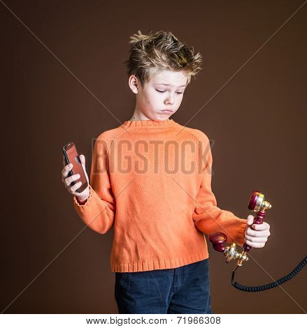 Confused boy holding one red retro rotary telephone in one hand and a cellular phone in the other. C