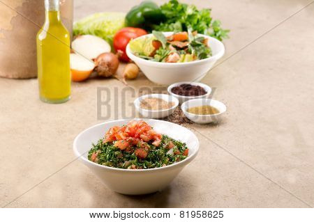 Plates of traditional Arabic salad fattouch and tabbouleh on a rustic background