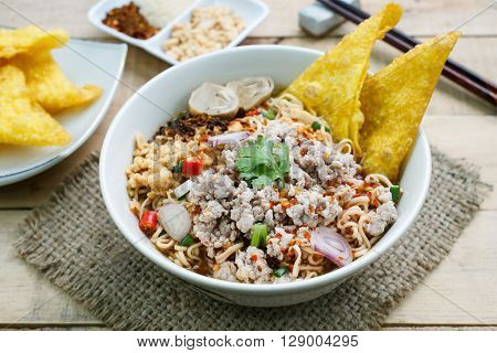 Spicy instant noodle soup with minced pork on wood background.