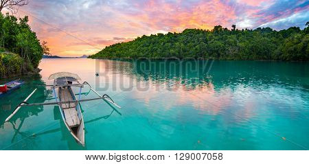 Breathtaking colorful sunset and traditional boat floating on scenic blue lagoon in the Togean (or Togian) Islands Central Sulawesi Indonesia upgrowing travel destination.