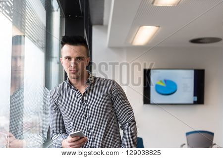 relaxed young businessman using smart phone at modern startup business office meeting room  with big window and city in backgronud
