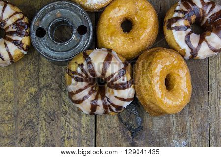 Close up top view of various dougnuts and vintage cutter isolated on rustic wood background