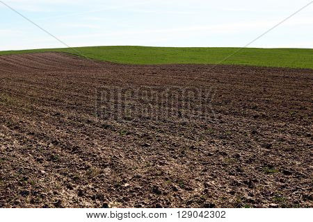 Arable land. Plowed field before planting. The brown earth and green grass on gorizonete. Rural landscape