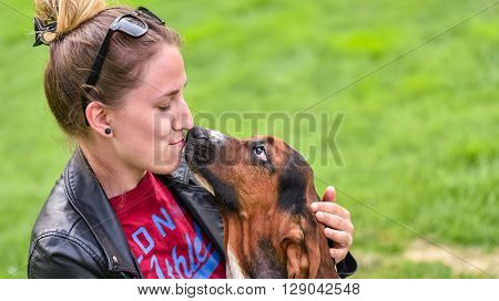 Young woman with an affectionate one year old Basset hound (Canis lupus familiaris) in the yard of a hobby farm.  Girl loves her dog, wet kisses from her one year old Basset hound.