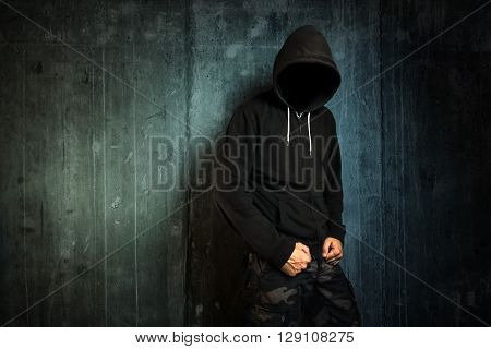 Dangerous unrecognizable faceless criminal standing in front of concrete wall crime rate and gangster lifestyle concept.