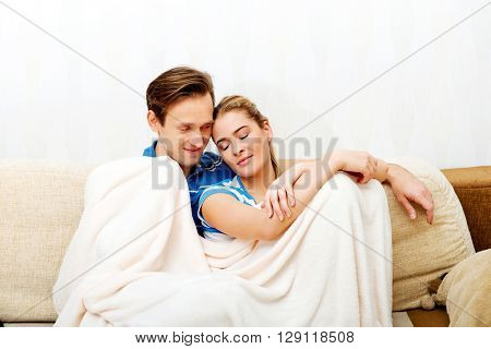 Smiling loving couple sitting on couch with blanket