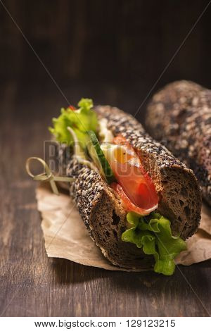 Tasty rye bread sandwhiches with ham, cheese and vegetables over dark wooden table