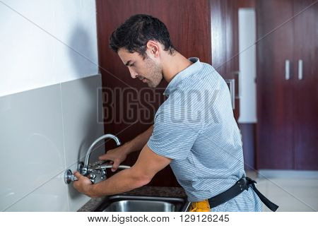 Man fixing faucet with wrench in kitchen