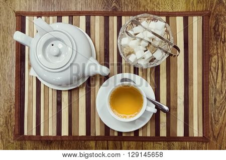 Top view of a cup of green tea teapot and sugar bowl on a wooden background