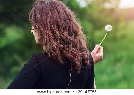 Beautiful girl standing with dandelion in hand