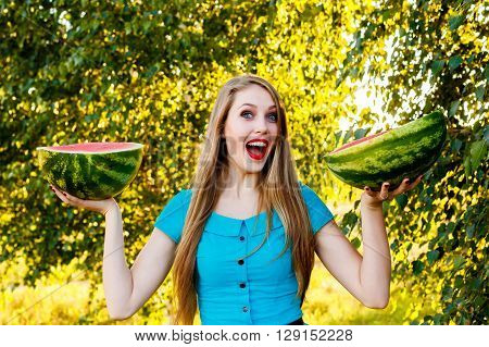 Beautiful blonde girl in a blue dress with long hair holding two halves of a sliced watermelon