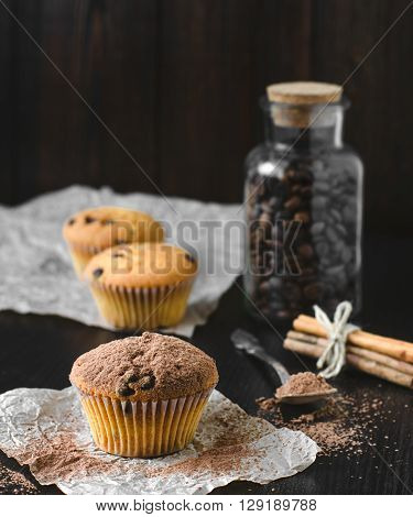 Cocoa muffins with coffee jar and cinnamon on dark background