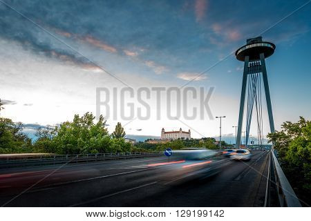 View on the Modern bridge with observation deck and restaurant called UFO and castle in Bratislava city at the sunset. Long exposure technique with motion of cars