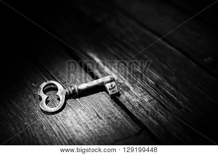 Rusty key on old wooden surface, black and white photo.