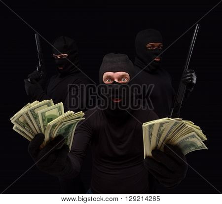 Portrait of gangster showing money stolen from house, apartment, flat, etc. Thieves in masks over black background. Isolated on black.