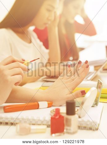 Closeup pictue of lady doing manicure, in particular painting nails while studying in library upon disciplines. Student and university concepts. Toned image.