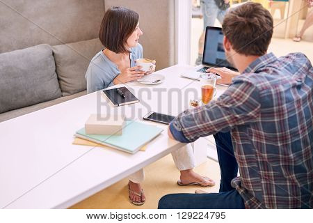 man busy showing his female business partner his budget proposal on his notebook while sitting in a public cafe drinking coffee and tea
