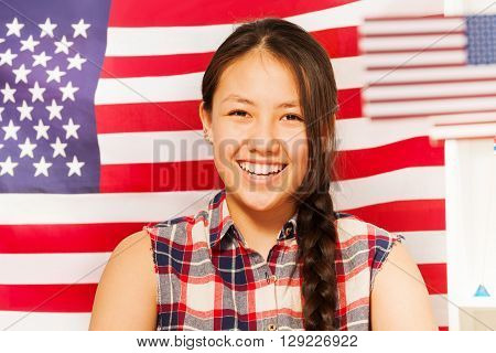Beautiful smiling teenage Asian girl with long plait against  the flag of United states of America