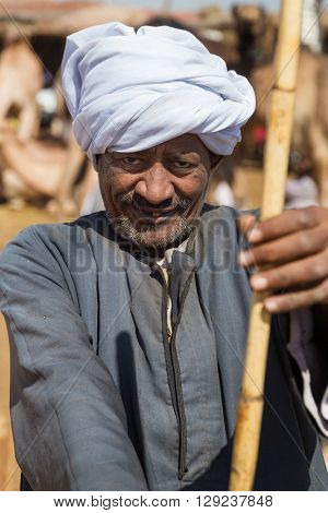 DARAW, EGYPT - FEBRUARY 6, 2016: Portrait of elderly camel salesman with stick at Camel market.