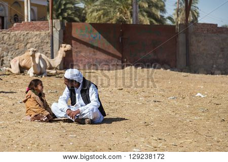 DARAW, EGYPT - FEBRUARY 6, 2016: Local camel salesmen and little girl sitting on the ground at camel market.