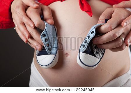 Young pregnant couple is holding baby shoes
