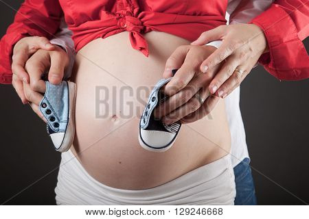 Young pregnant couple is holding baby shoes