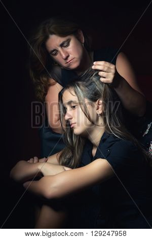 Troubled and sad teenage girl with her worried mother trying to comfort her