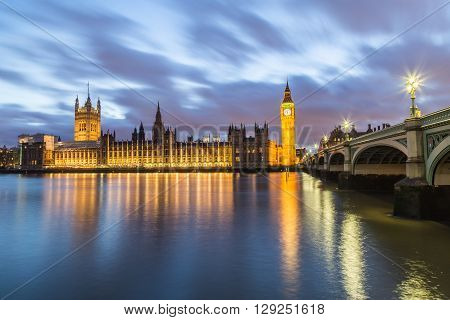 Houses of Parliament from across the River Thames at dusk. Part of Westminster Bridge can be seen.